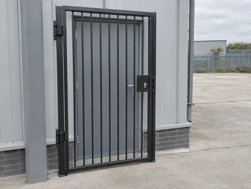 Black hinged steel security gate with a lock box in front of a commercial back door